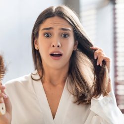 Shocked Young Woman Worried About Hairloss After Brushing Hair In Bathroom, Upset Female Holding Comb Full Of Fallen Hair And Looking At Camera With Despair, Emotionally Reacting To Health Problems